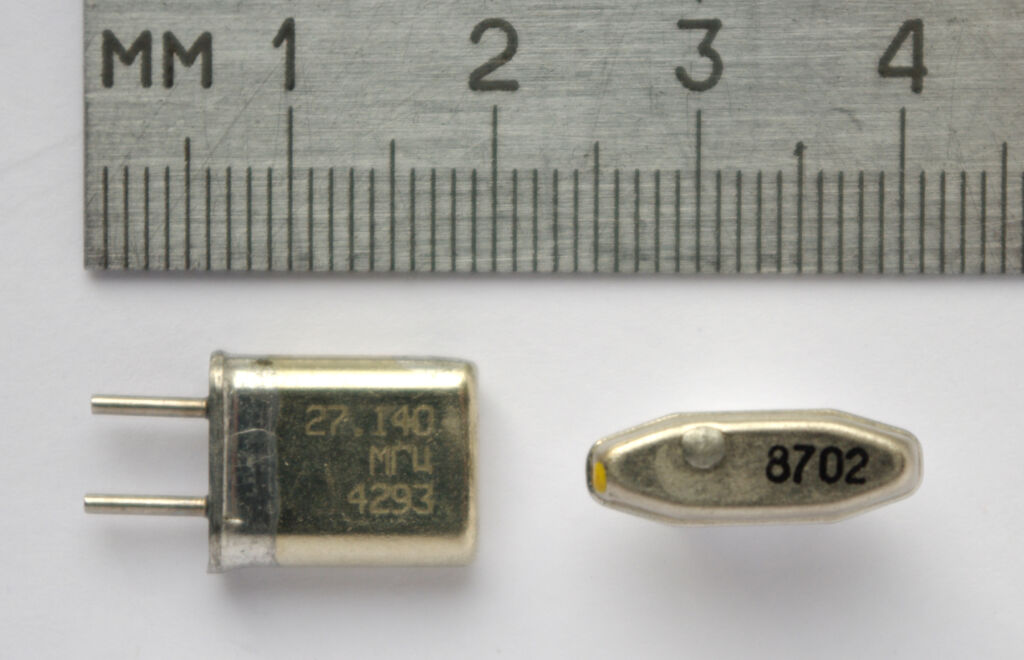 Un risonatore al quarzo accanto a un righello: dentro c'è una sottile lamina di cristallo che vibra a una frequenza cost