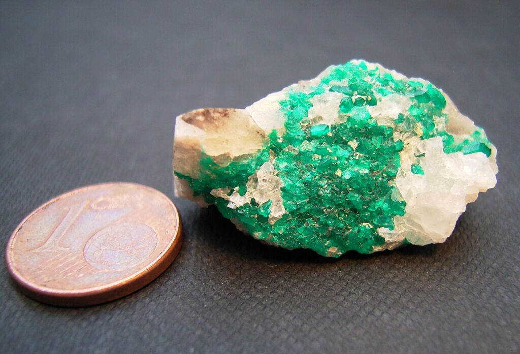Cristalli di dioptasio accanto a una moneta, per dare un'idea delle dimensioni: il verde intenso viene dal rame.