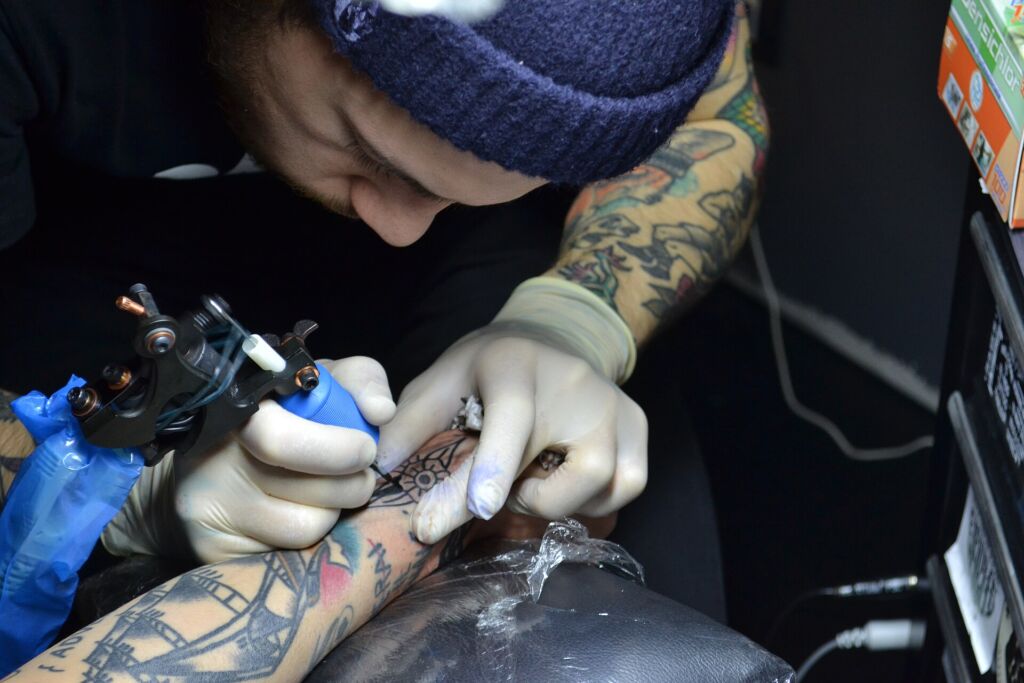 Un tatuatore al lavoro: guanti, aghi monouso e inchiostri a norma sono le prime cose da controllare in uno studio.