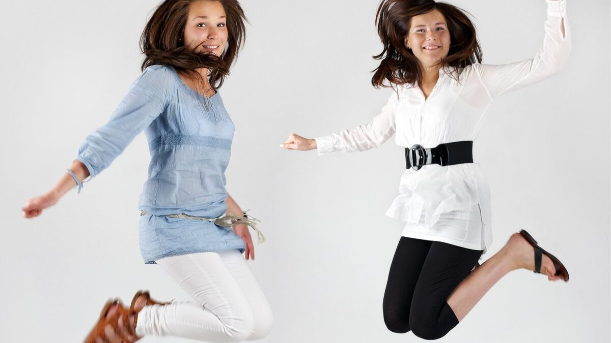 Due ragazze saltano, una indossa pantaloni bianchi